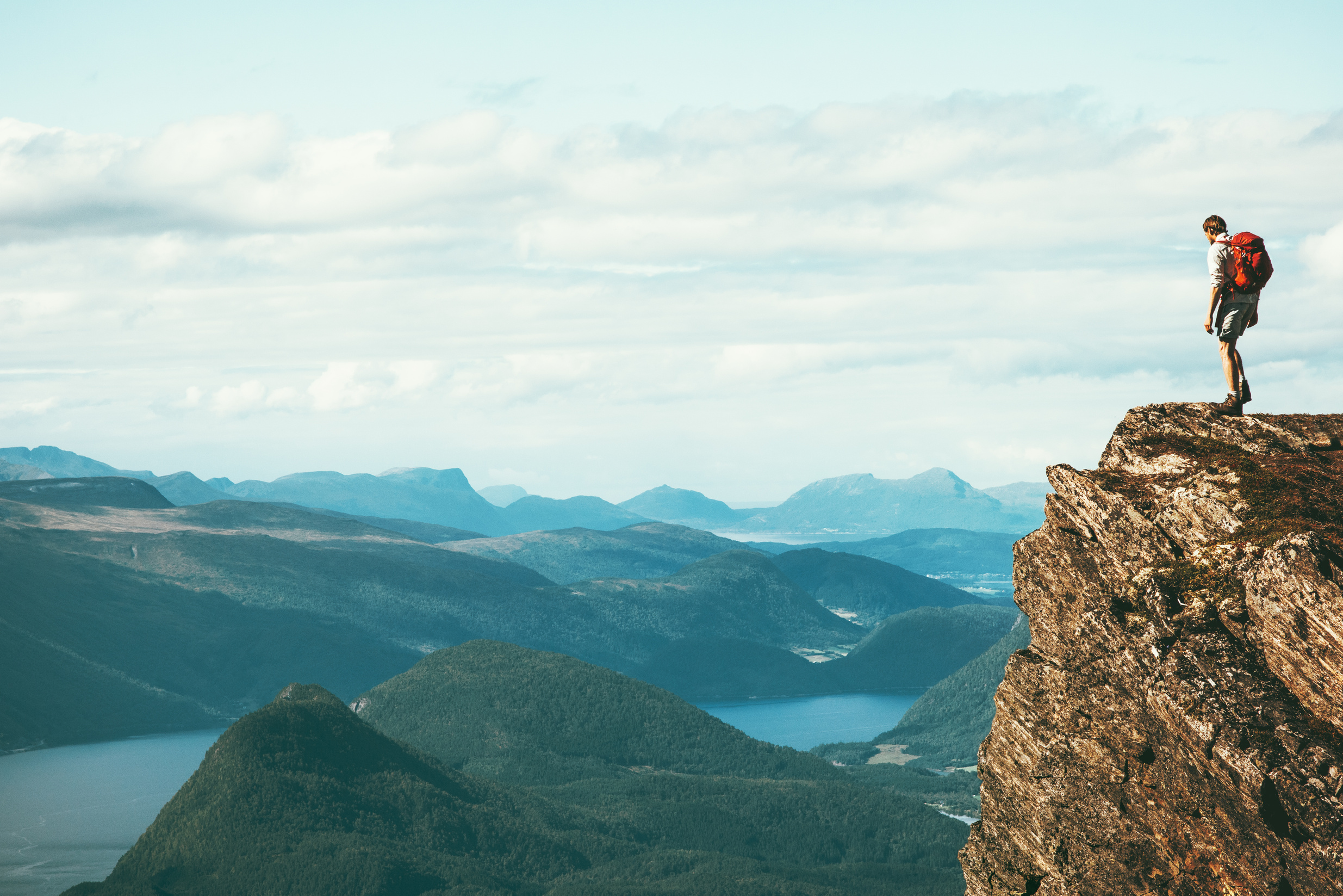 Man explorer standing on cliff alone mountain summit over fjord Norway landscape Travel Lifestyle success motivation concept adventure active vacations outdoor